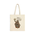 Natural canvas tote with Taco the raccoon beneath “Here for the living” lettering and a woodland flower bouquet.