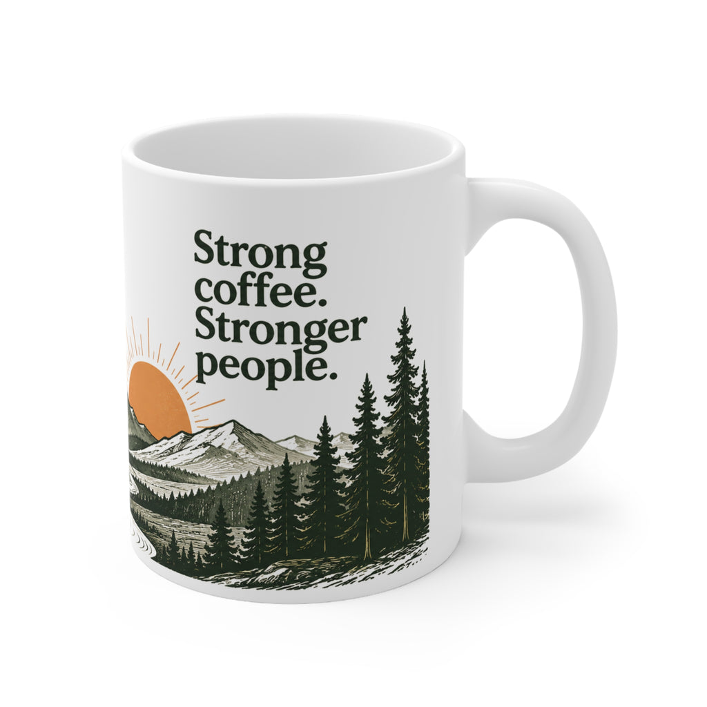 White ceramic mug with “Strong coffee. Stronger people.” text above a vintage mountain, pine forest, winding road, and terracotta sunrise illustration.
