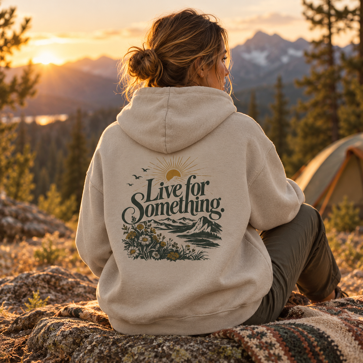 Woman wearing the oat gray Live for Something oversized graphic hoodie at a mountain campsite, with the back artwork clearly visible.